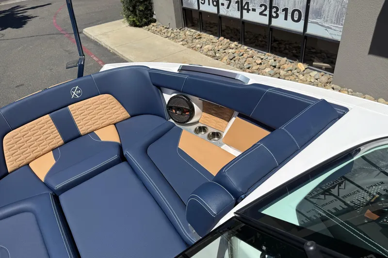 Slide: The Image of 2024 MasterCraft X24 boat interior with blue and tan seating, cup holders, and speaker. - 30