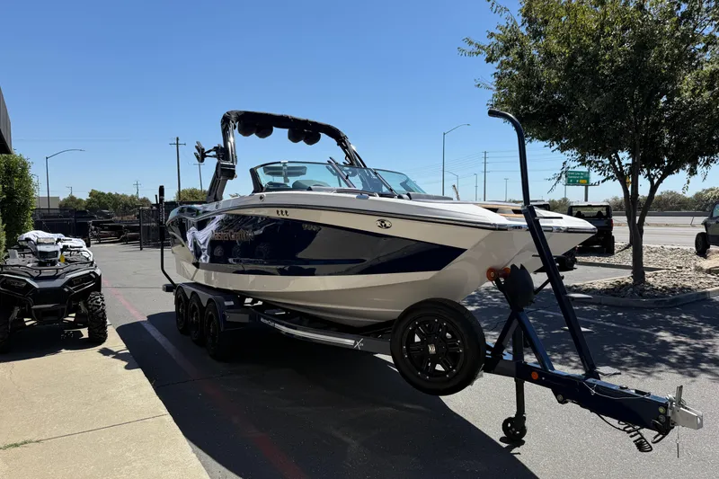 Slide: The Image of 2024 MasterCraft X24 boat on trailer, parked outdoors near trees and vehicles. - 6