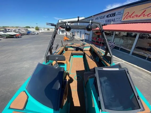 Slide: The Image of 2022 Axis Wake Research T250 boat with teal and wood accents, parked at a dealership. - 14