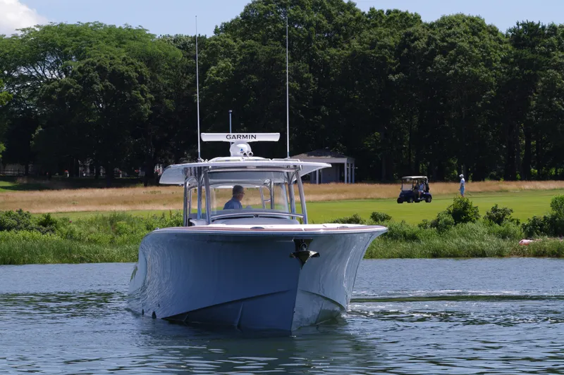 Slide: The Image of 2025 Mag Bay 43 CC boat cruising on a calm lake near a golf course. - 15