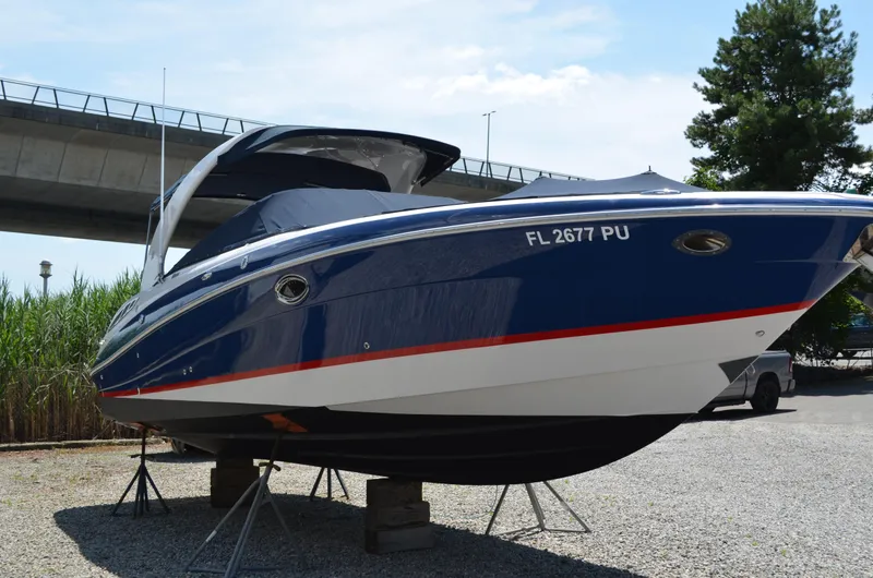 Slide: The Image of 2013 Four Winns H310 boat on stands, blue hull with red stripe, under a bridge. - 2