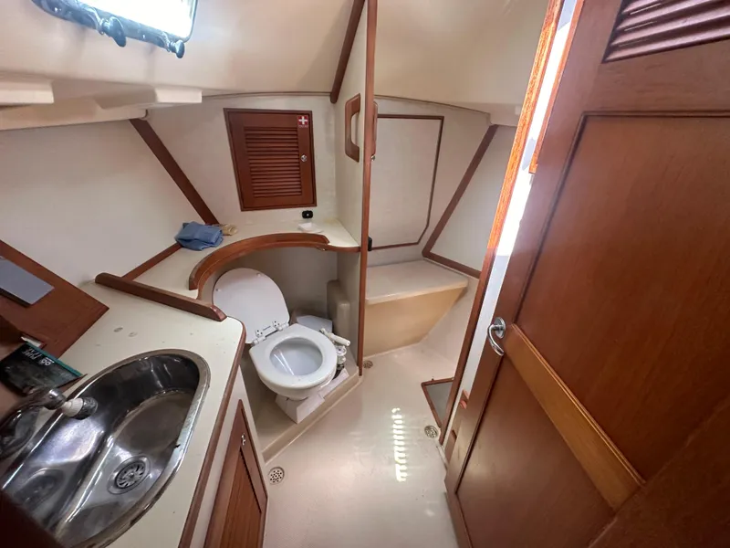 Slide: The Image of 2002 Island Packet 420 yacht bathroom with sink, toilet, and wooden cabinetry. - 25
