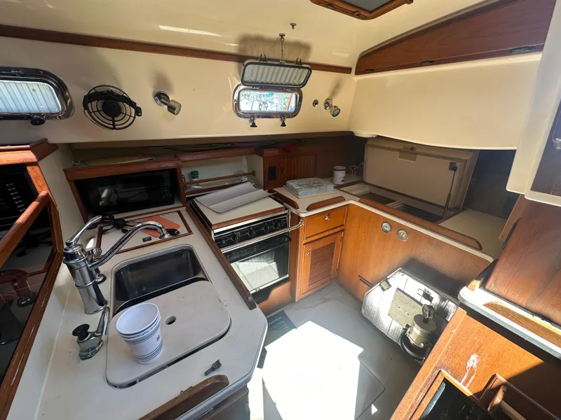 Slide: The Image of 2002 Island Packet 420 sailboat galley with stove, sink, and wooden cabinetry. - 38