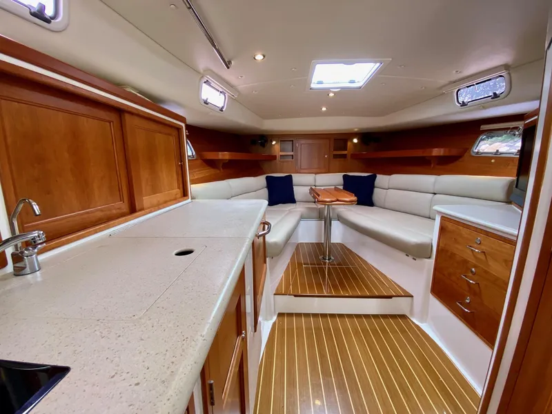 Slide: The Image of 2013 MJM 36z Downeast boat interior with plush seating and wooden accents, docked by a scenic shoreline. - 18