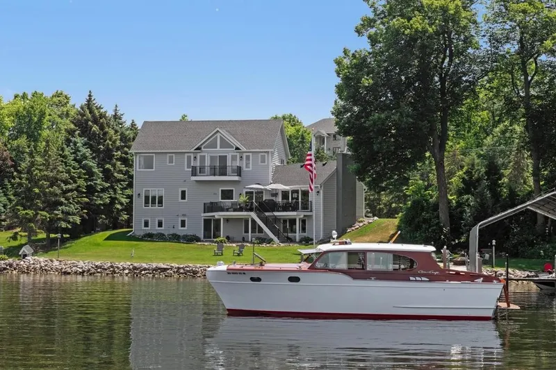 Slide: The Image of 1954 Chris-Craft Sedan Cruiser on a serene lake near a modern lakeside home. - 3