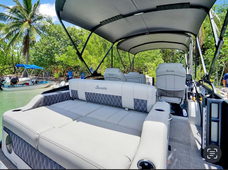 Slide: The Image of 2022 Barletta Lusso 25UC pontoon boat with luxurious seating, docked near lush greenery. - 3