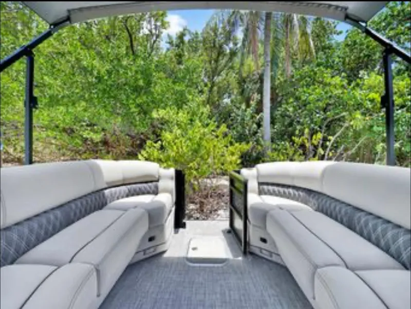 Slide: The Image of 2022 Barletta Lusso 25UC pontoon boat interior with plush seating and scenic greenery backdrop. - 8
