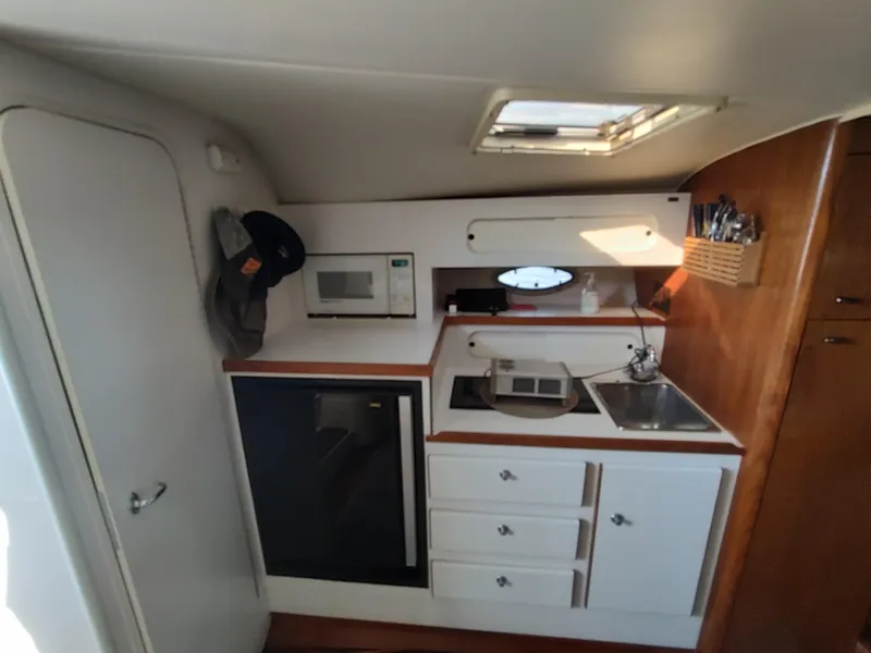 Slide: The Image of Compact kitchen area inside a 1994 Tiara Yachts 3100 Open, featuring a microwave, sink, and storage. - 5