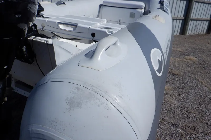 Slide: The Image of 2015 Walker Bay 325 STX Odyssey inflatable boat, gray exterior, docked on gravel surface. - 4