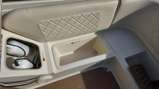 Slide: The Image of 2017 Chris-Craft 27 Launch boat interior with beige seating and black canopy in a garage. - 12