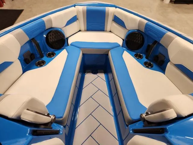Slide: The Image of 2023 Malibu 26 LSV boat interior with blue and white seating, cup holders, and speakers. - 34