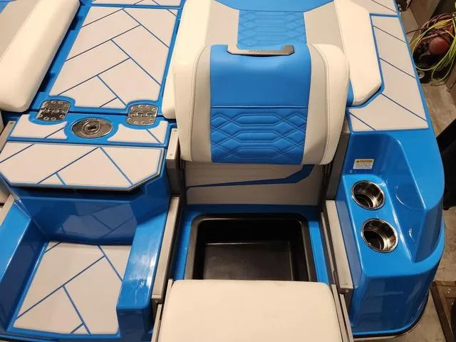 Slide: The Image of 2023 Malibu 26 LSV boat interior with blue and white seating, cup holders, and storage. - 36