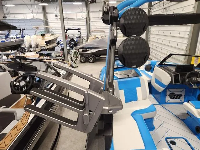 Slide: The Image of 2023 Malibu 26 LSV boat interior with blue and white seating, wakeboard rack, and speakers. - 37