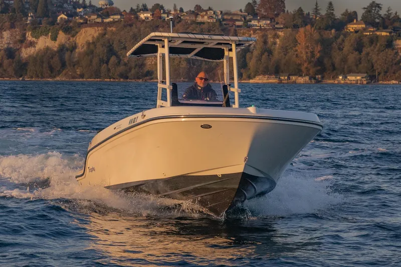 Slide: The Image of 2022 Bayliner Trophy T22CC boat cruising on a scenic lake with a wooded shoreline. - 2