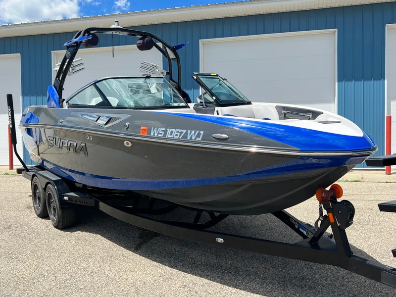 Slide: The Image of 2015 Supra SG 400 boat on trailer, blue and gray, parked outside a blue building. - 1