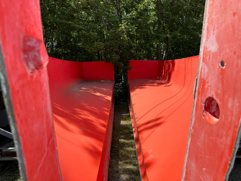 Slide: The Image of Red Calvin Beal MOLDS boat hulls, 2024 model, set outdoors among trees. - 10