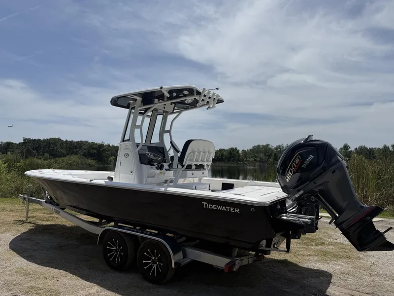 Slide: The Image of 2024 Tidewater 2410 Bay Max boat on trailer, parked near a lake under a cloudy sky. - 32