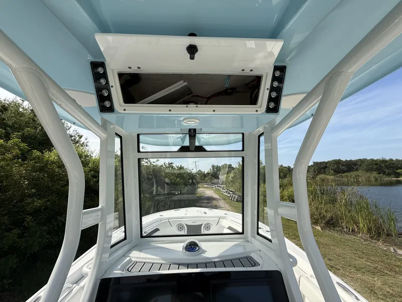 Slide: The Image of 2024 Tidewater 256 CC Adventure boat interior with console and windshield, near a scenic waterway. - 18