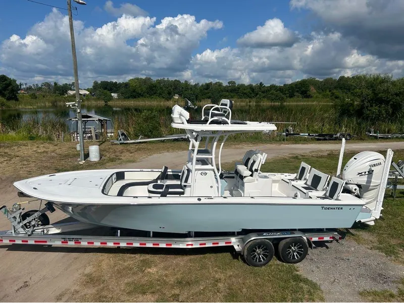 Slide: The Image of 2025 Tidewater 2700 Carolina Bay boat on trailer, parked near a lake under a partly cloudy sky. - 7