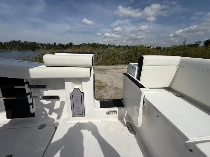 Slide: The Image of 2024 Tidewater 256 LXF boat interior with seating and footrest, near a lake under a blue sky. - 17