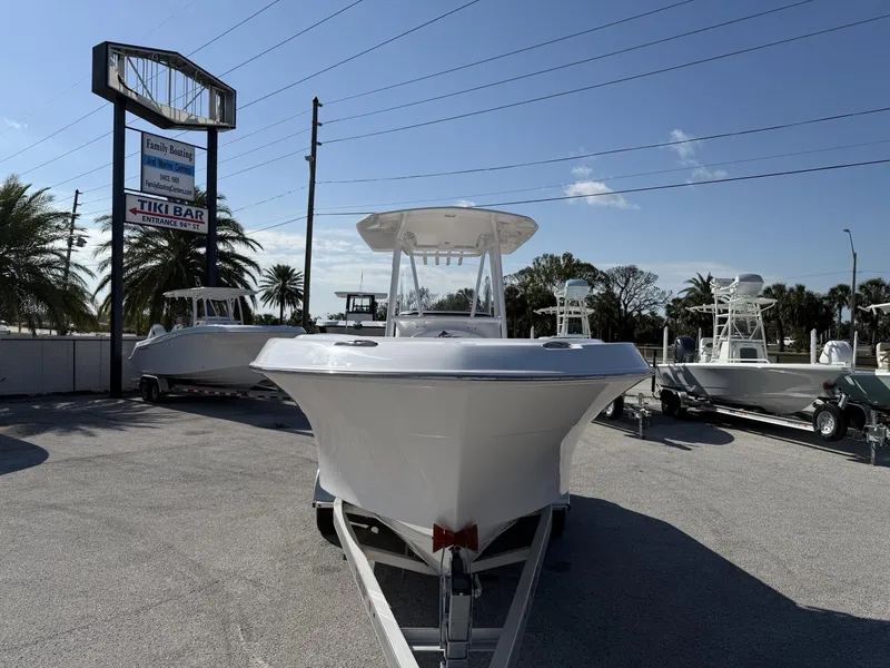 Slide: The Image of 2024 Aquasport 2300 CC boat on trailer at dealership, sunny day, palm trees in background. - 24