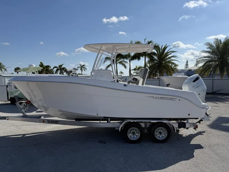 Slide: The Image of 2024 Aquasport 2300 CC boat on trailer, sunny day, palm trees in background. - 3