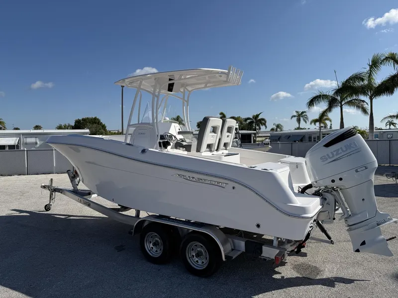 Slide: The Image of 2024 Aquasport 2300 CC boat on trailer with Suzuki outboard motor, palm trees in background. - 4