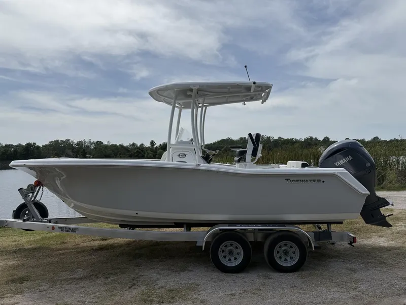 Slide: The Image of 2024 Tidewater 220 CC Adventure boat on trailer, parked near a lake under cloudy sky. - 17