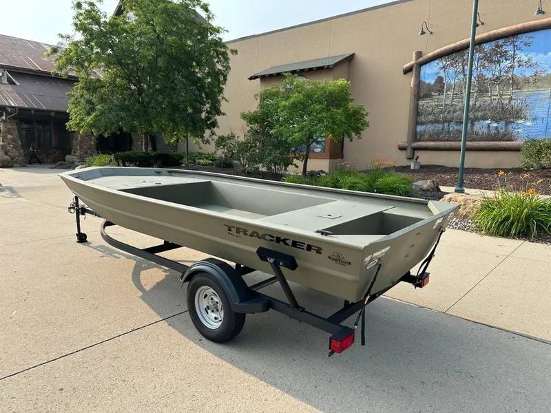 Slide: The Image of 2024 Tracker Grizzly 1754 Jon boat on trailer, parked outdoors near a building. - 2