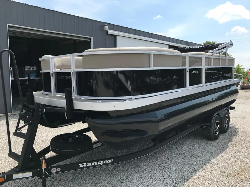 Slide: The Image of 2024 Ranger Reata 200C pontoon boat on a trailer outside a garage. - 2