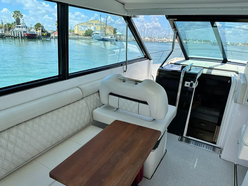 Slide: The Image of 2023 Regal Grande Coupe interior with white seating and wooden table, overlooking marina. - 5