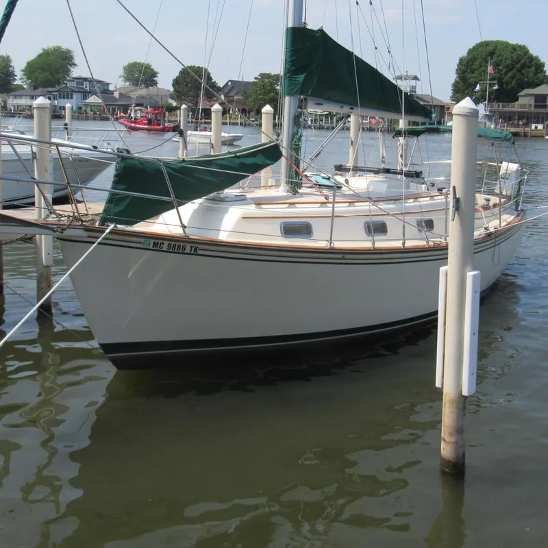 The Image of 1987 Island Packet 31 sailboat docked in a marina with green covers. - 0