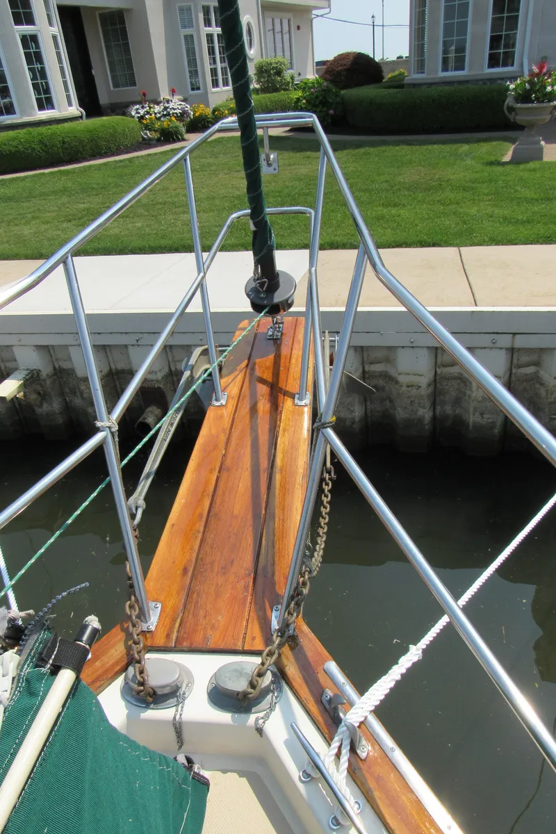 Slide: The Image of 1987 Island Packet 31 sailboat bow with polished wood and metal railings, docked near a garden. - 17