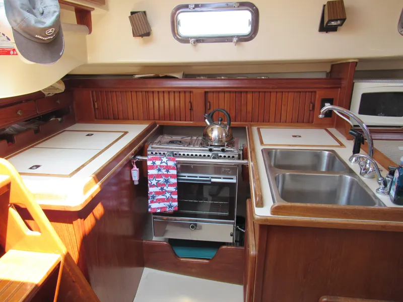 Slide: The Image of Cozy 1987 Island Packet 31 yacht kitchen with stove, sink, and wooden cabinetry. - 6