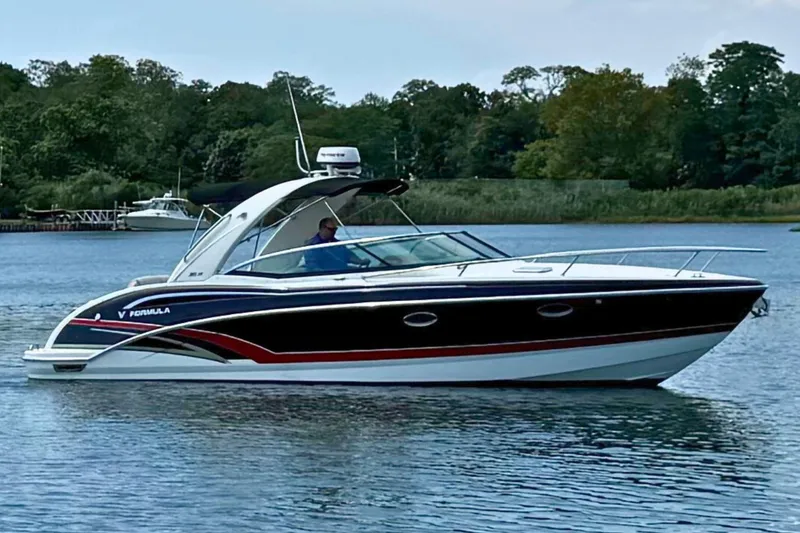 Slide: The Image of 2015 Formula 310 Sun Sport boat cruising on a serene lake with lush greenery. - 5