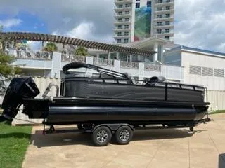 Slide: The Image of 2024 Regency 230 DL3 pontoon boat on trailer, parked near modern building. - 2