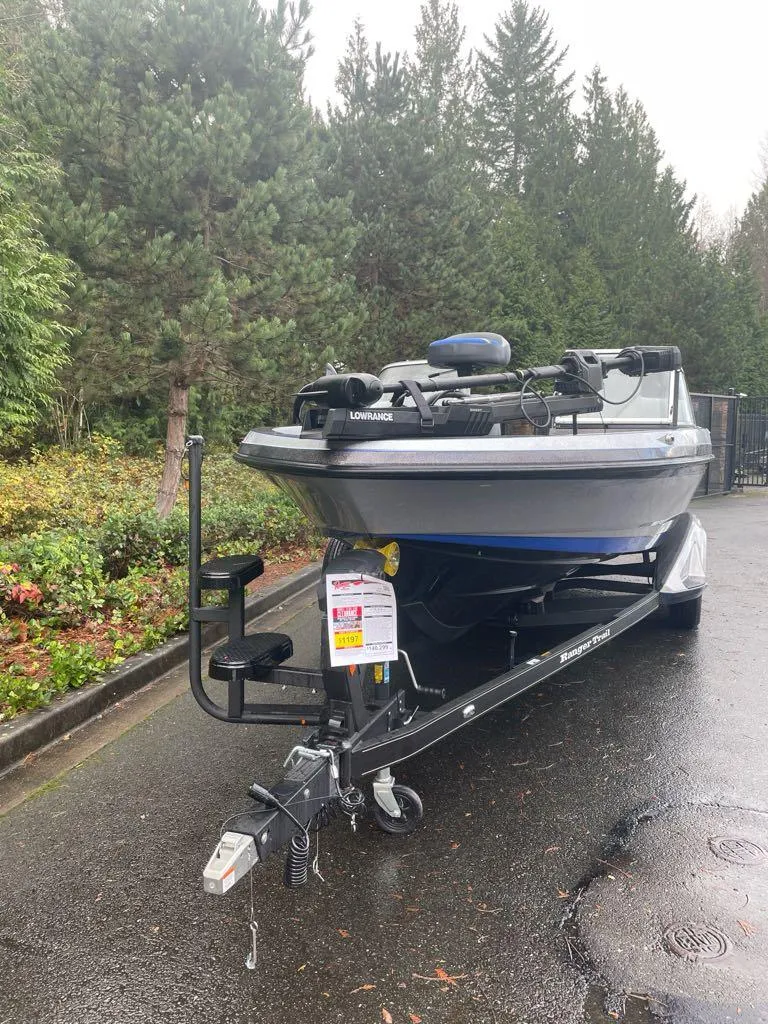 Slide: The Image of 2024 Ranger 621FS Pro boat on trailer, parked on wet pavement, surrounded by trees. - 7