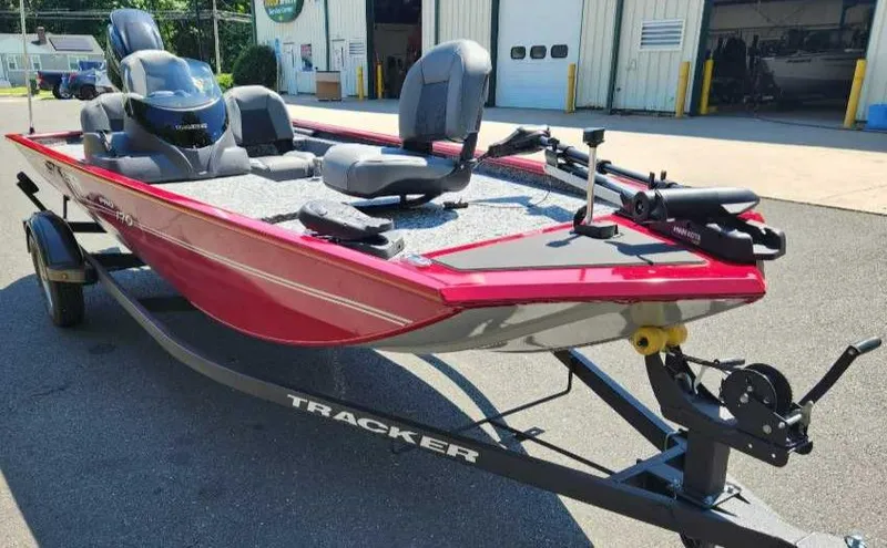 Slide: The Image of 2024 Tracker Pro 170 boat on trailer, red exterior, parked outside a garage. - 2