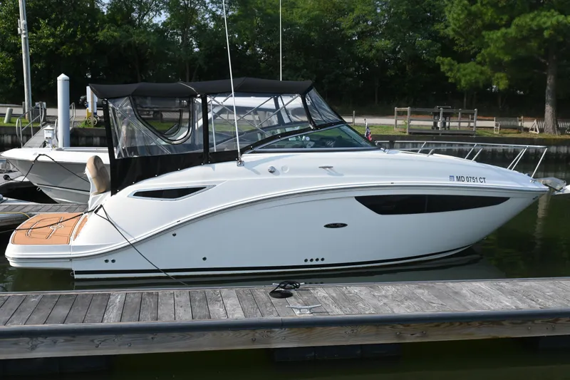 Slide: The Image of 2018 Sea Ray Sundancer 260 docked at marina, featuring sleek white design and black canopy. - 0