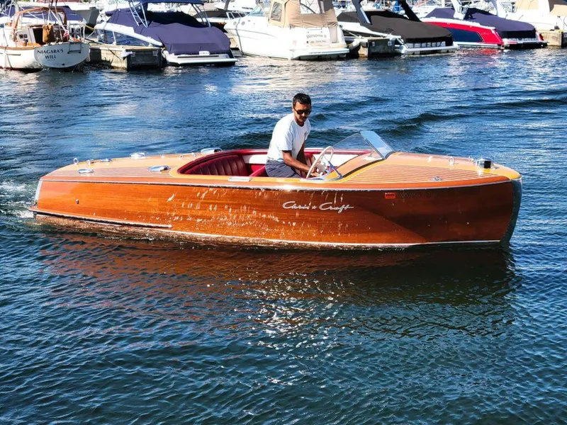 The Image of 1951 Chris-Craft Riviera 16 classic wooden boat on water with man at helm. - 0