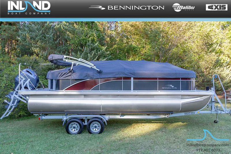 Slide: The Image of 2023 Bennington 22 SL pontoon boat on a trailer, covered and parked on grass. - 22
