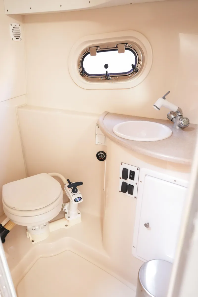 Slide: The Image of 2004 Four Winns Vista boat bathroom with toilet, sink, and porthole window. - 14