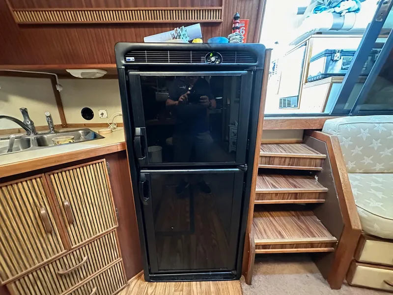 Slide: The Image of 1986 Sea Ray 390 Express Cruiser kitchen with black refrigerator and wooden cabinetry. - 19