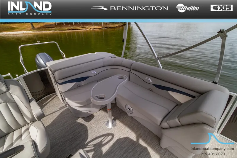 Slide: The Image of 2023 Bennington 20 SLM pontoon boat interior with plush seating and table on a lake. - 21