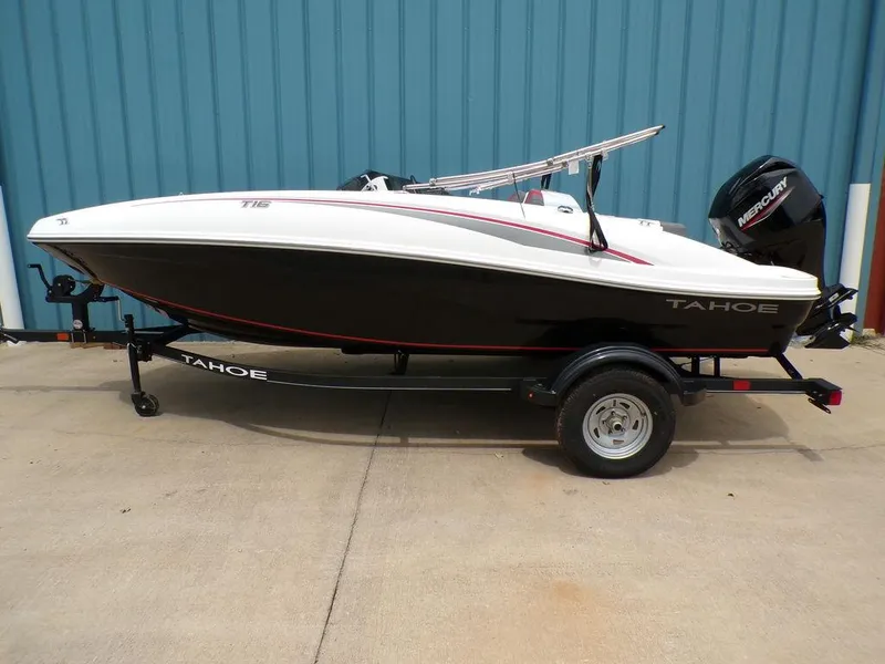 The Image of 2024 Tahoe T16 boat on trailer, black and white design, parked by blue wall. - 1