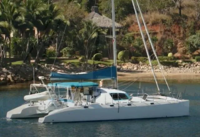 Slide: The Image of 2000 Ocean Cat 49 catamaran anchored near a tropical shoreline with lush greenery. - 1