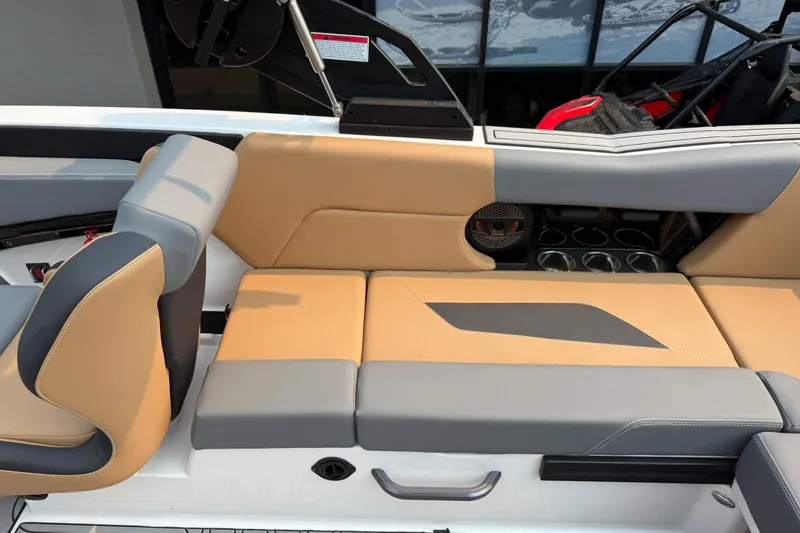 Slide: The Image of 2024 MasterCraft NXT23 boat interior with tan and gray seating, cup holders, and speaker. - 16