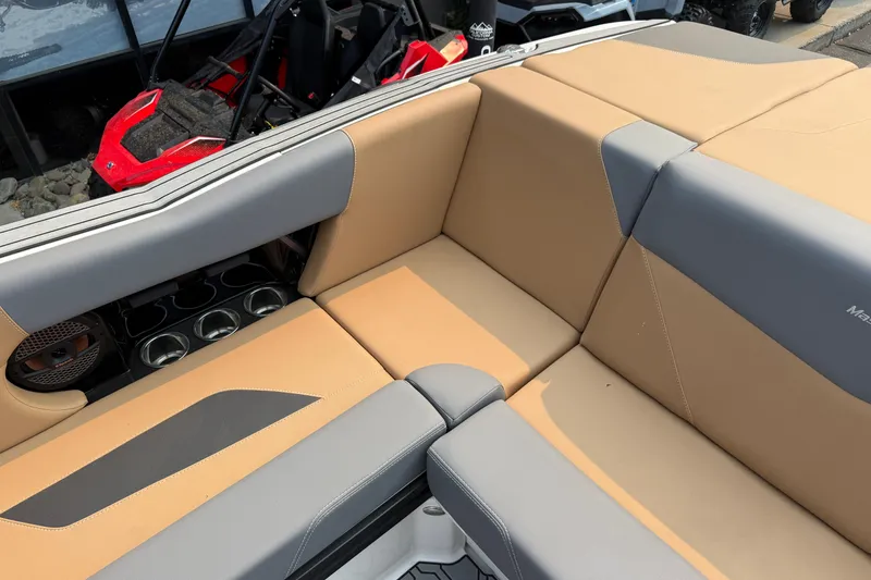 Slide: The Image of 2024 MasterCraft NXT23 boat interior with tan and gray seating, cup holders, and speaker. - 17