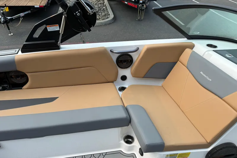 Slide: The Image of 2024 MasterCraft NXT23 boat interior with tan and gray seating, featuring branded upholstery. - 21