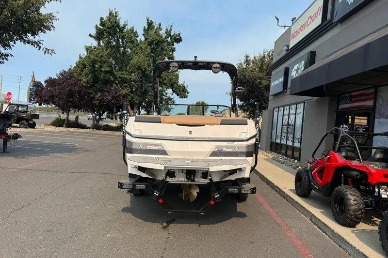 Slide: The Image of 2024 MasterCraft NXT23 boat displayed outside dealership, rear view with trees and vehicles nearby. - 4